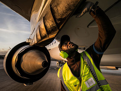 Black man wearing safety vest, underneath an airplane