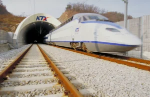 A high-speed rail train comes out of a tunnel. A high-speed rail track is seen. The KTX logo is on the tunnel.